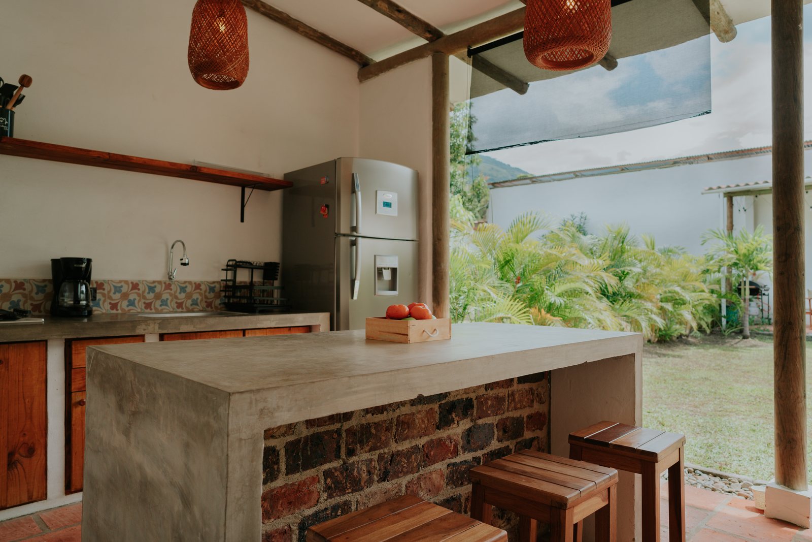 Cocina abierta de Casa UIRA con isla de concreto y ladrillo, bancos de madera y ventanal al jardín