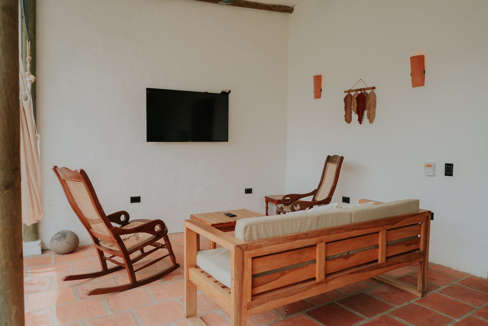 Sala con Smart TV, mecedora y sofá de madera sobre piso de baldosa de barro