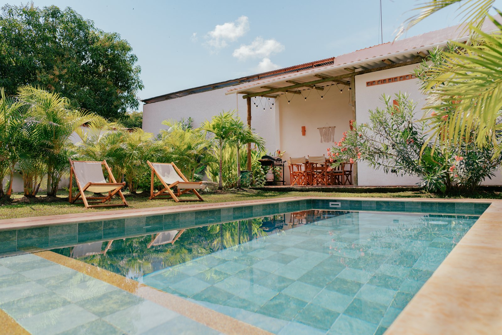 Piscina privada de mosaico verde con tumbonas de madera y lona, rodeada de palmeras