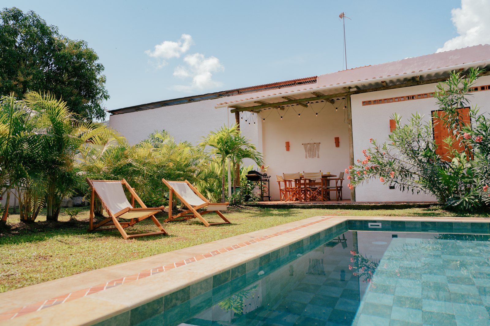 La piscina vista desde el jardín, con el comedor exterior y la casa blanca al fondo