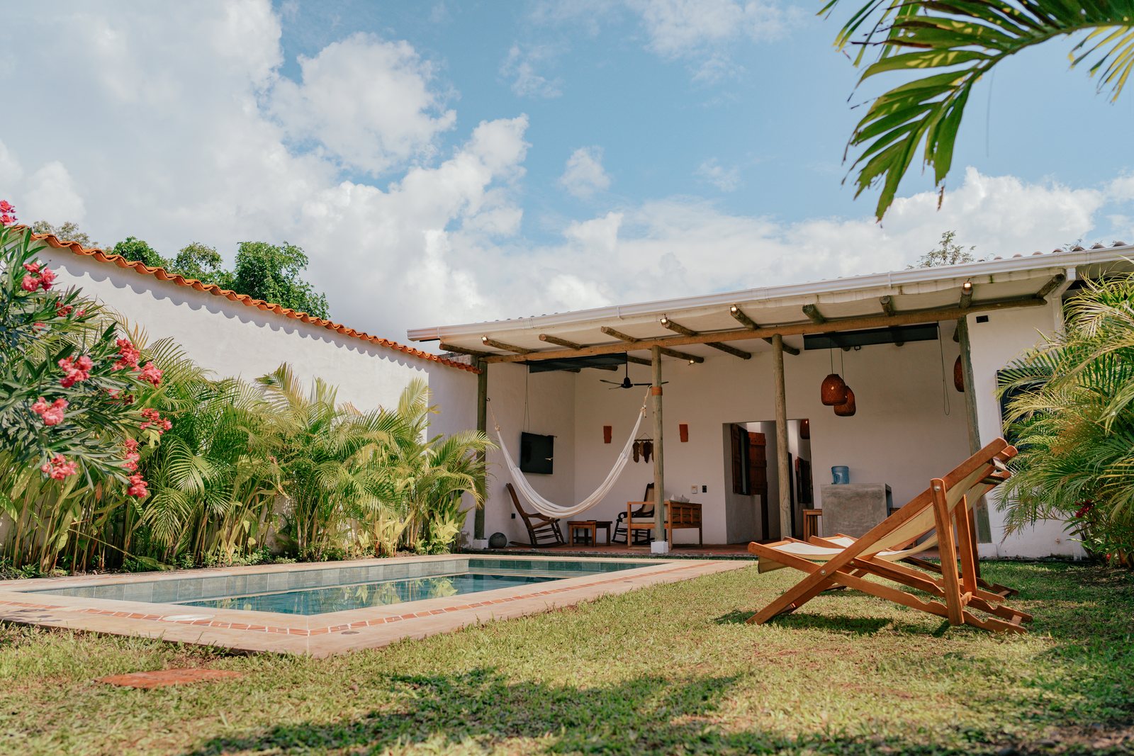 Piscina con una hamaca colgada en el corredor y una silla de playa sobre el césped