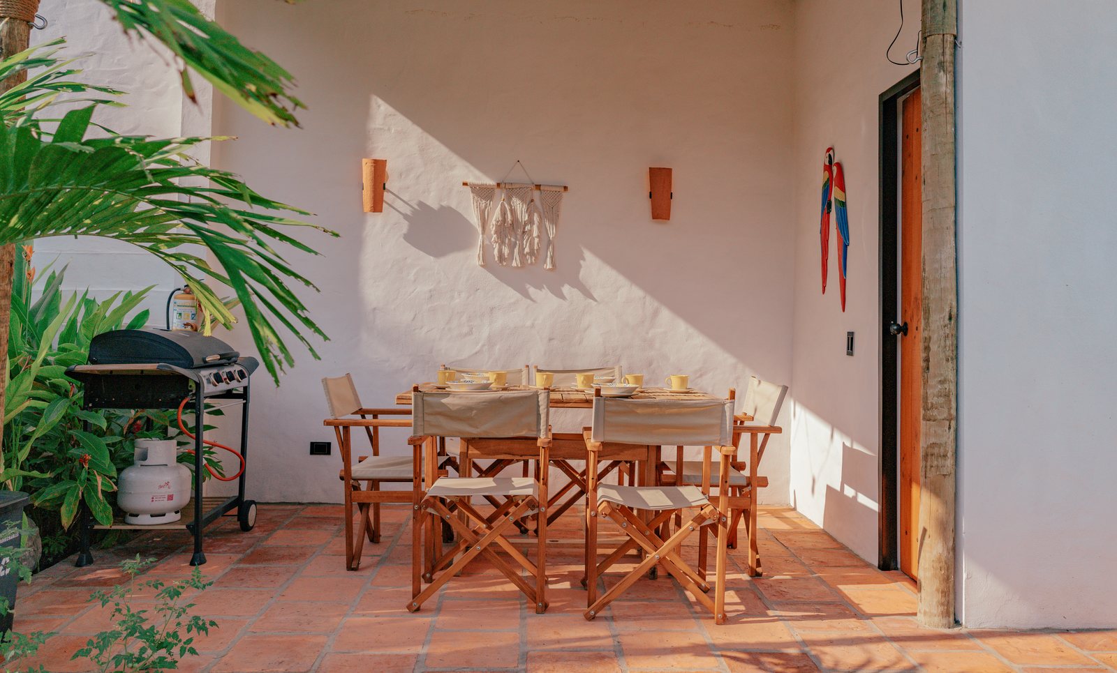 Comedor exterior de madera para ocho personas bajo el corredor techado, junto al asador