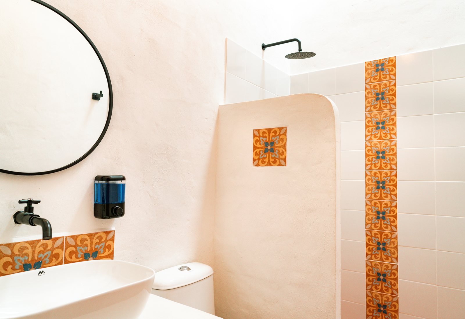 Baño privado con ducha de lluvia, espejo redondo y detalles en baldosa artesanal naranja