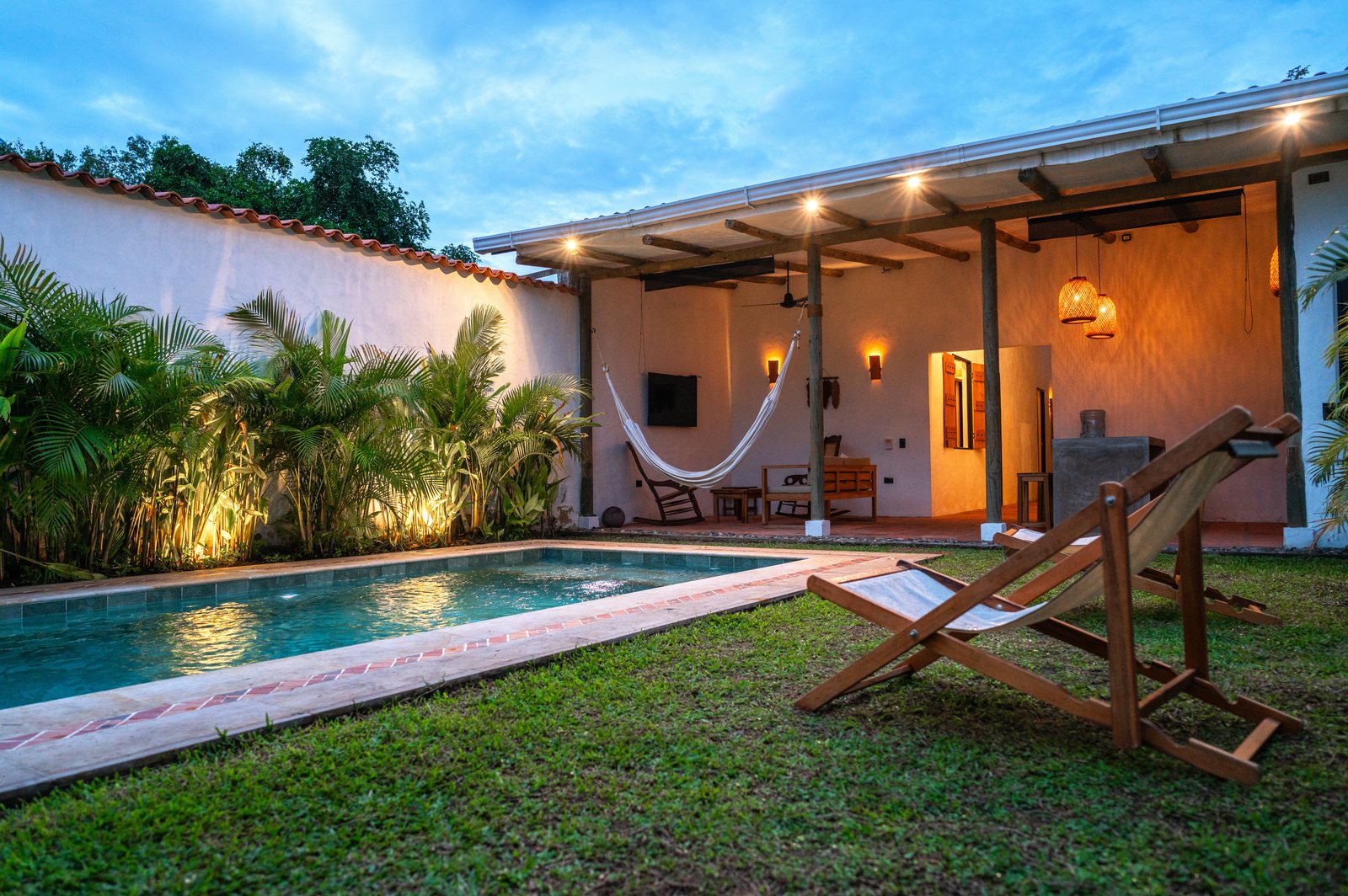 La piscina iluminada al atardecer, con la hamaca del corredor encendida al fondo