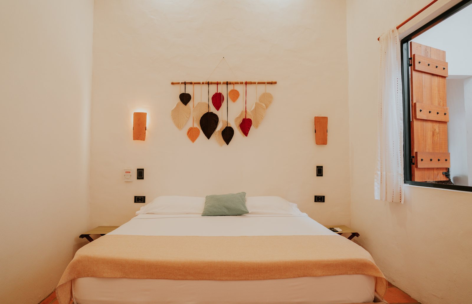 Habitación con cama queen, móvil artesanal y ventana con postigos de madera