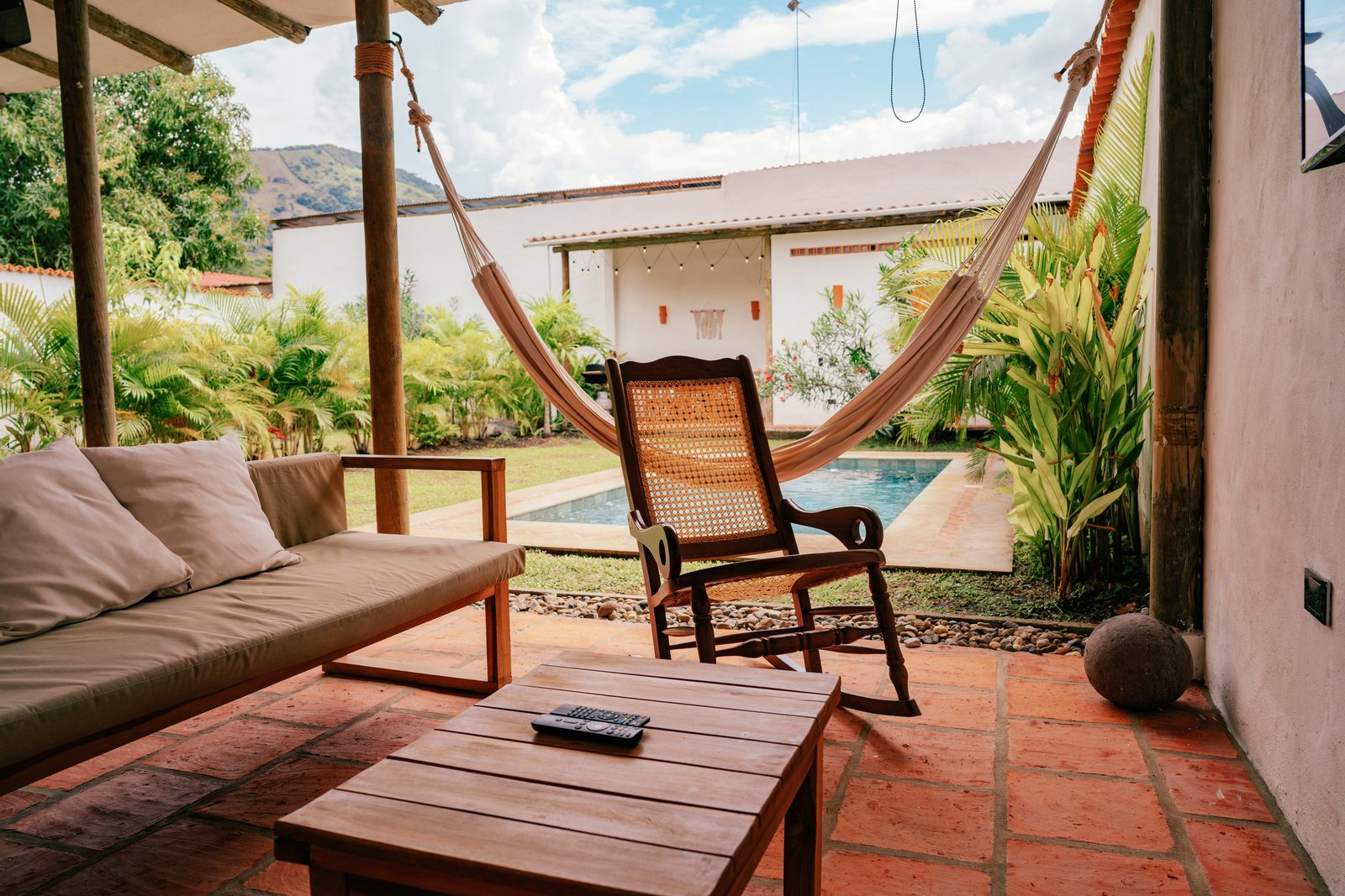 Terraza con sofá, mesa baja de madera y mecedora frente a la piscina